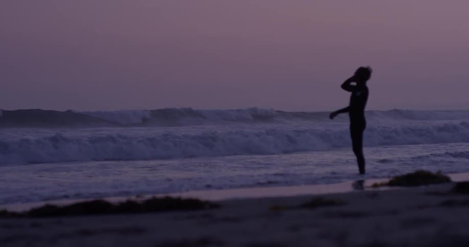 Surfer watches ocean on the beach at sunset