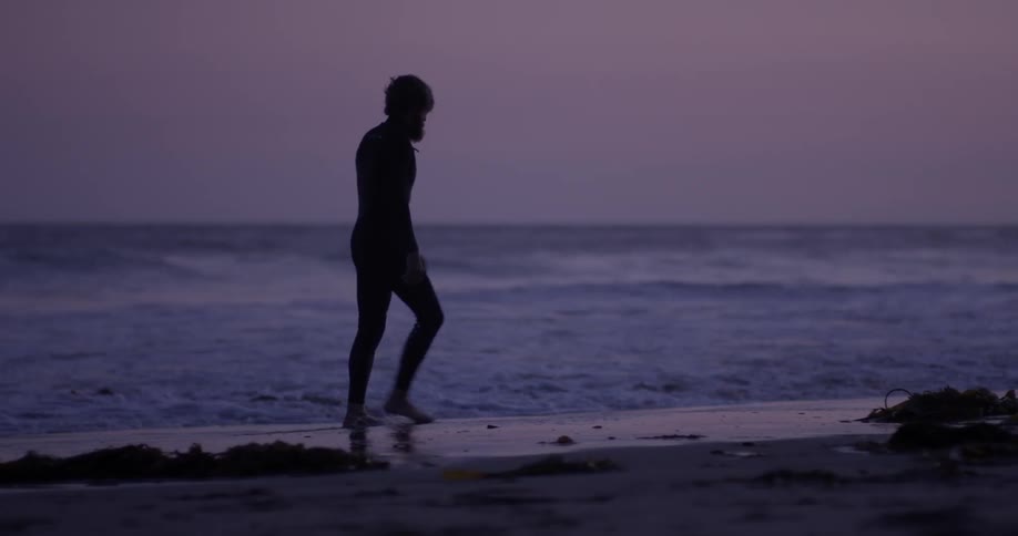 A man walks on a beach as waves rush onto the sand at his feet
