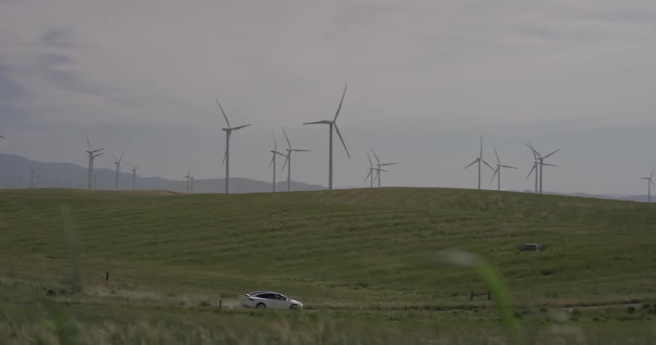 A car drives down a rural road near spinning windmills