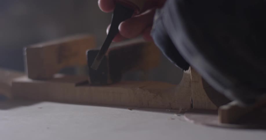 A man that is using a chisel on a piece of wood