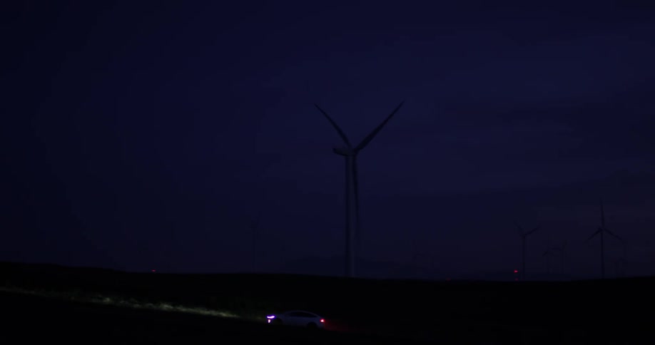 Car drives near spinning windmills at night