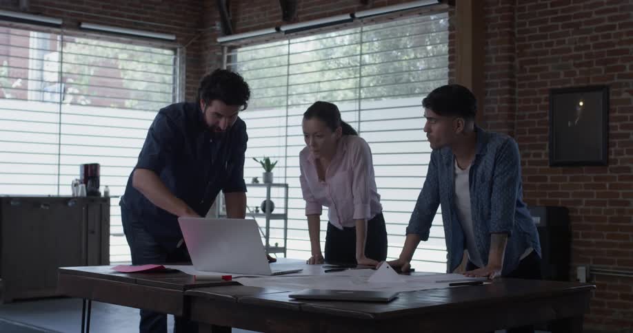 Two men and one woman looking at something on a laptop in an office