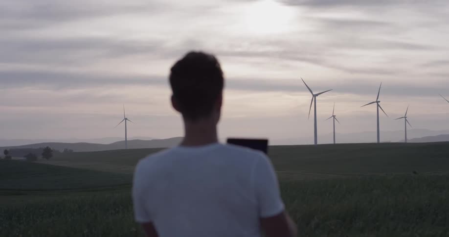 Man stands in a field observing windmills at a wind farm