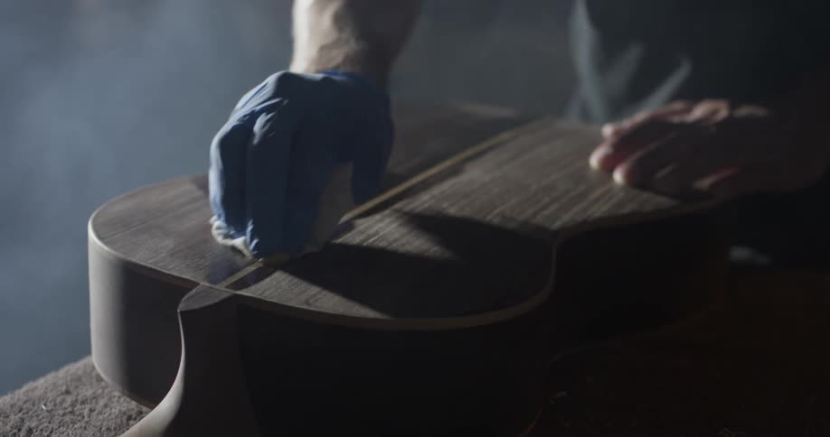 A person staining a piece of wood that is on a guitar