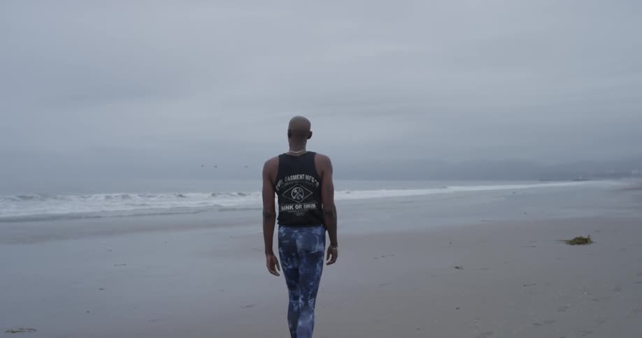 A man walks along a beach under an overcast sky as waves roll in