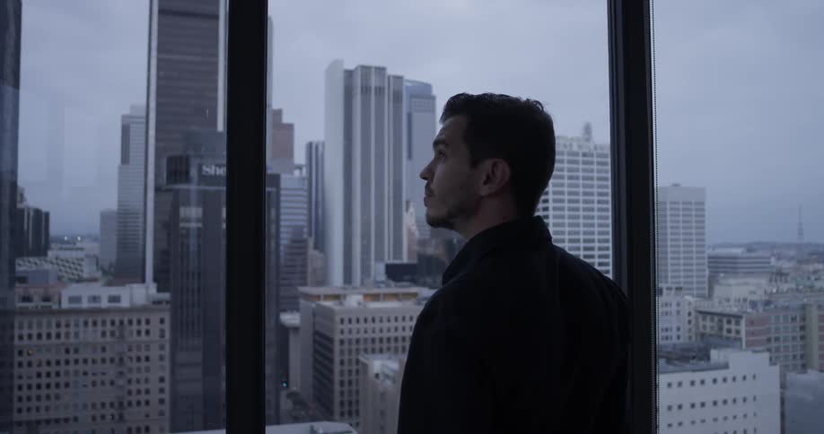 Man stares out of high-rise windows then turns and walks away