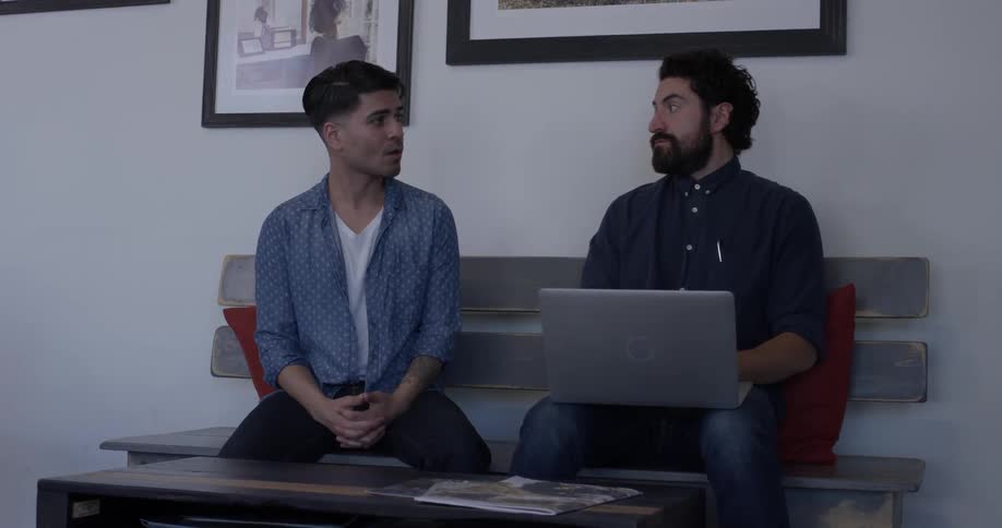 Two men sitting on a bench talking and looking at a laptop