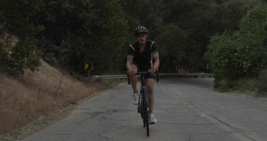A man riding his bike up a hill on an empty road surrounded by trees