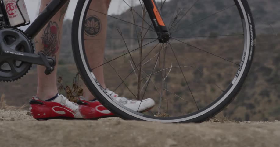 A man standing on a dirt path while holding his bicycle