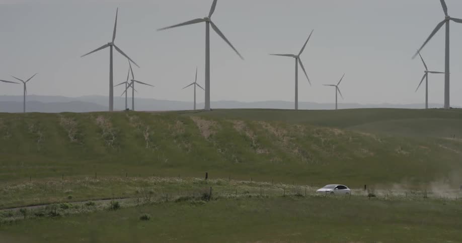 Car drives down the road near windmills a sunny day