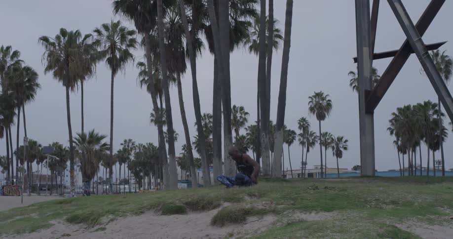A man mediates outside near palm trees