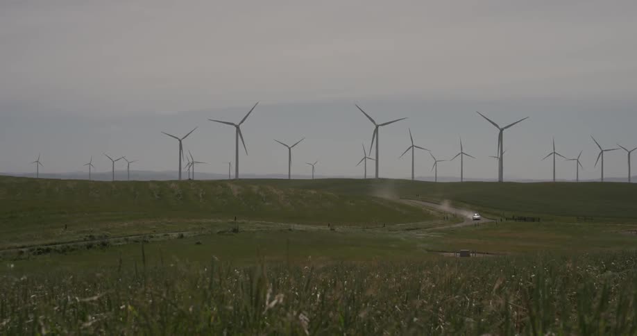 A car driving on a dirt road through a windmill field