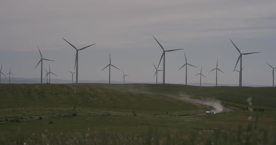 A car driving down a dusty road with rotating windmills