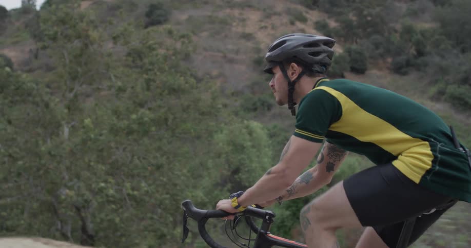 A man in a green and yellow shirt,black shorts, and a black helmet is bike riding near mountains