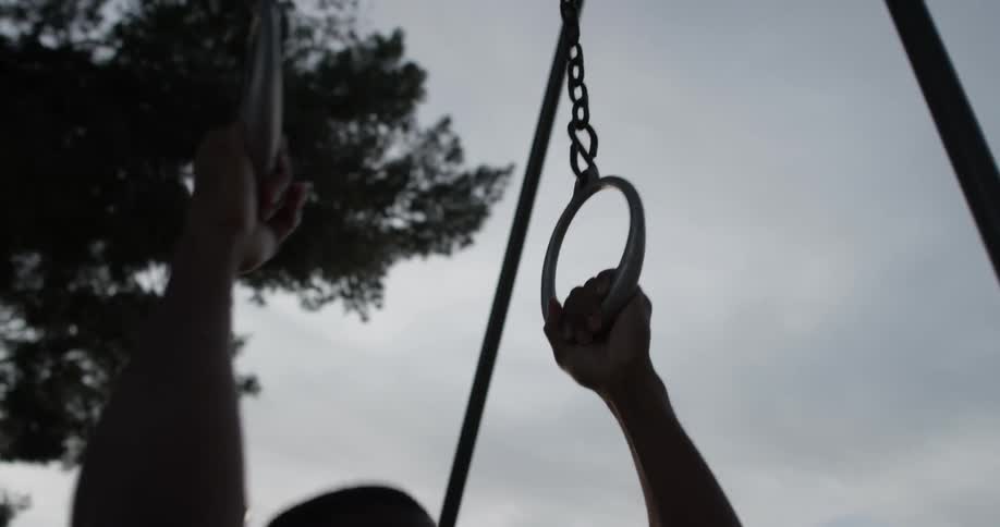 A man using gymnast rings to do pull ups