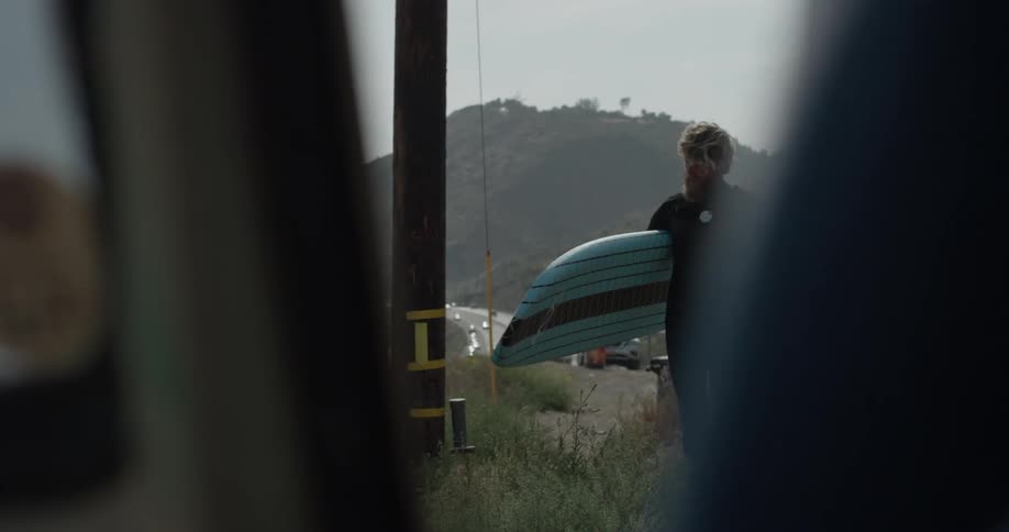 A man walks through a grassy area holding a surfboard