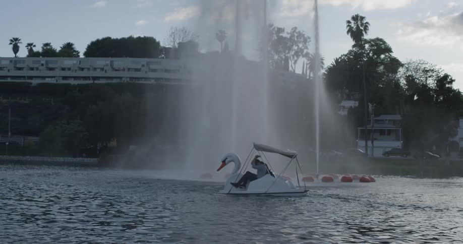 A man and woman peddling a swan boat next to a fountain