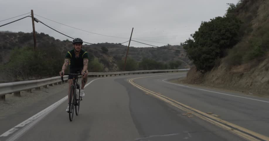 Man riding a bike on an empty road surrounded by hills