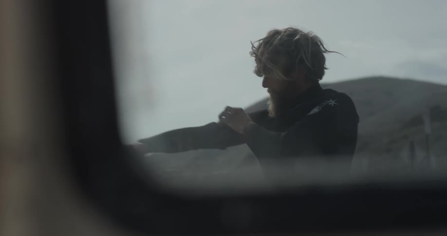 A man taking off a wetsuit next to a car