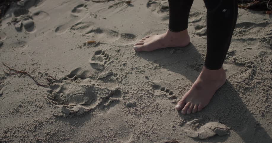 Someone stands on the sand in  a wet suit