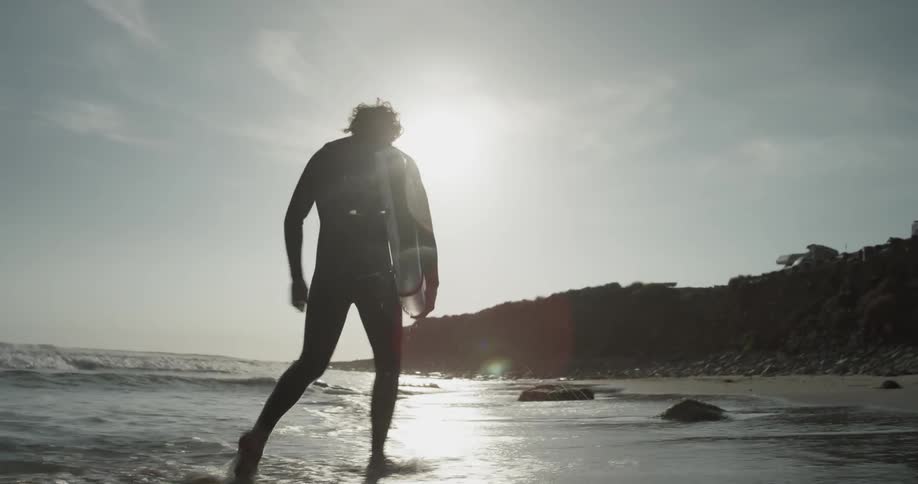 A man with a surfboard walks through the water