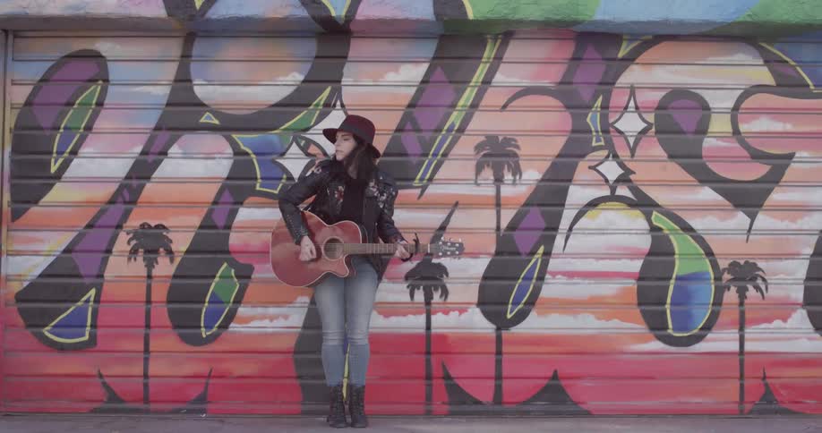 Woman playing the guitar in front of a graffiti wall