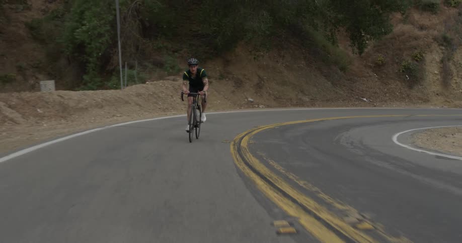 A man riding his bike up a steep road surrounded by cliffs