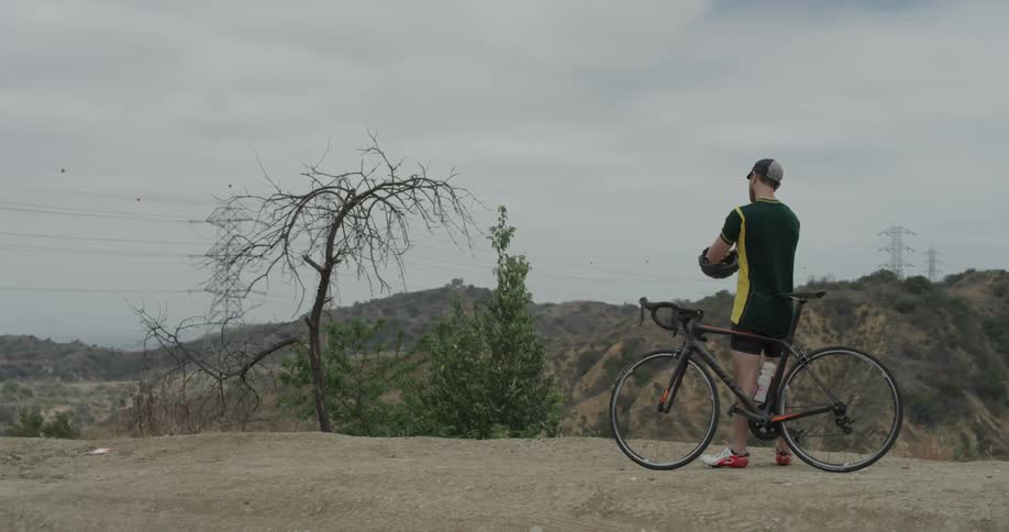 A man taking off his bicycle helmet at the top of a mountain