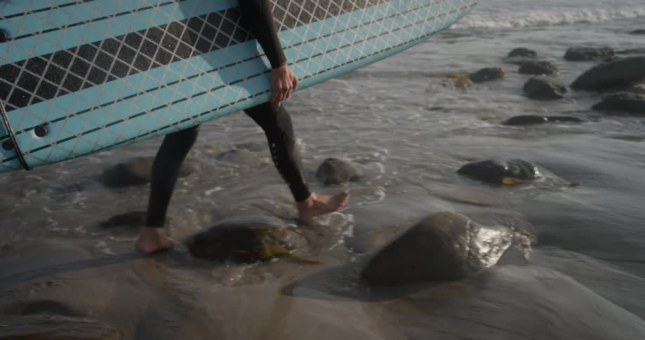 A man holding a surfboard walks along the water edge