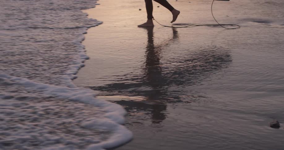 A person walking along the shore with a surfboard