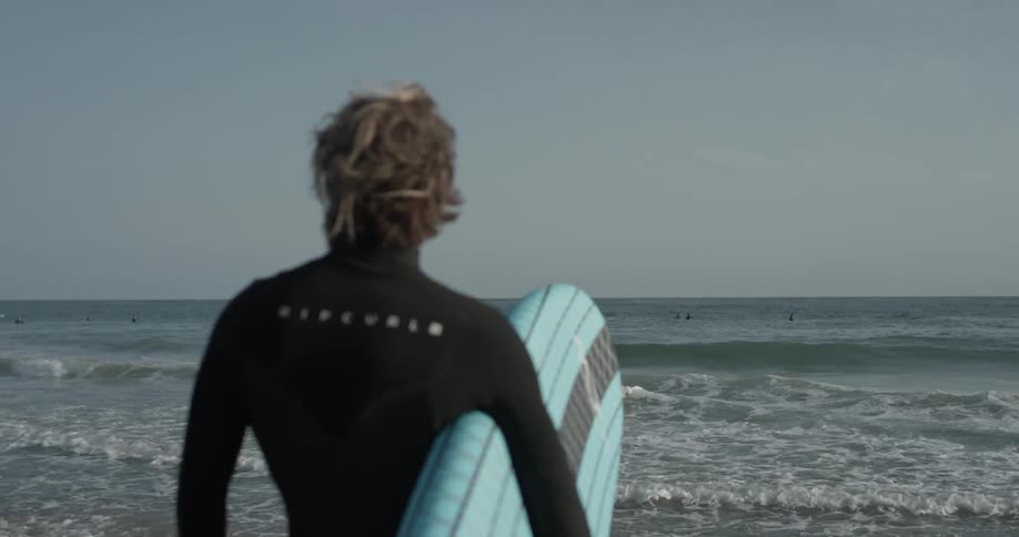 A man carrying a surfboard next to the beach with waves crashing