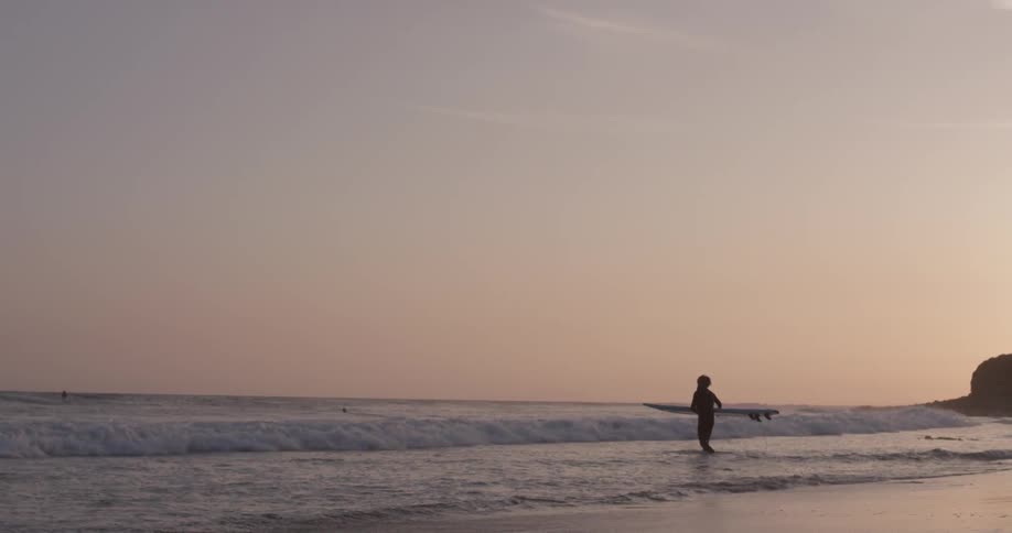 A man that is carrying a surfboard into the ocean