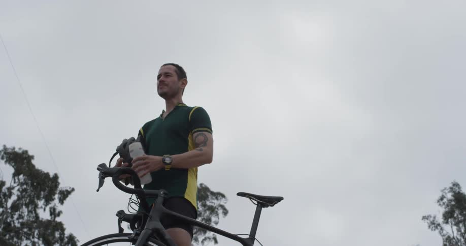 A man standing next to a bike drinking water from a water bottle