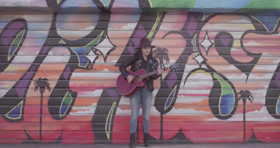 A woman standing playing a guitar in front of a mural