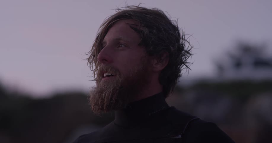 A man with a beard wearing a wetsuit at dusk