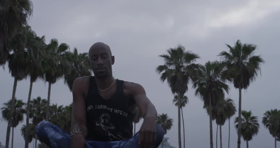 Man sits down on ground with palm trees in the background