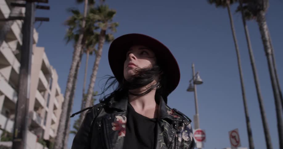A woman in a hat walking down a sidewalk wearing a hat