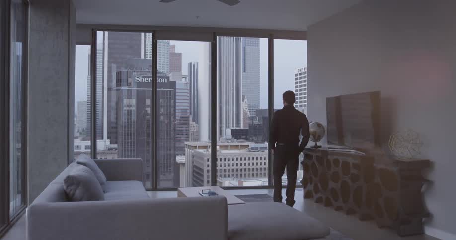 Man walks toward the tall windows in a high-rise apartment