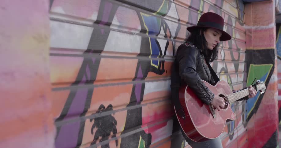 A woman standing on the sidewalk that is playing a guitar