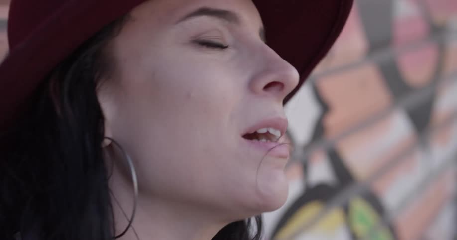 A woman in a hat singing while standing next to a mural