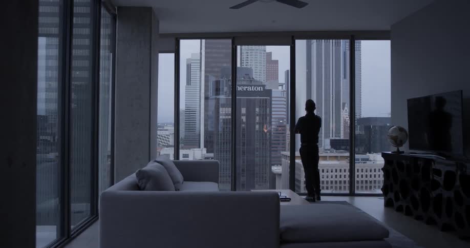 A man looking out an apartment window at a city