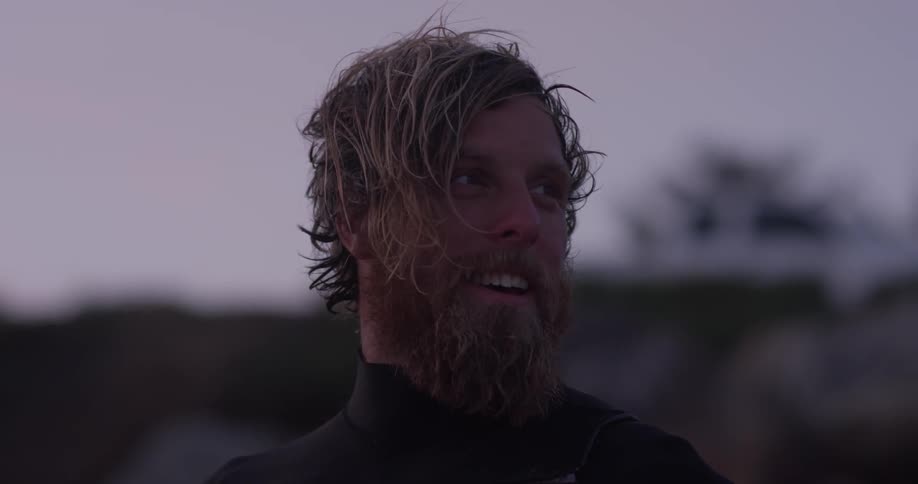 A bearded man turns and smiles while standing on a beach