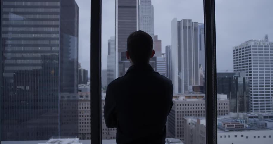 A man looks out a window at skyscrapers
