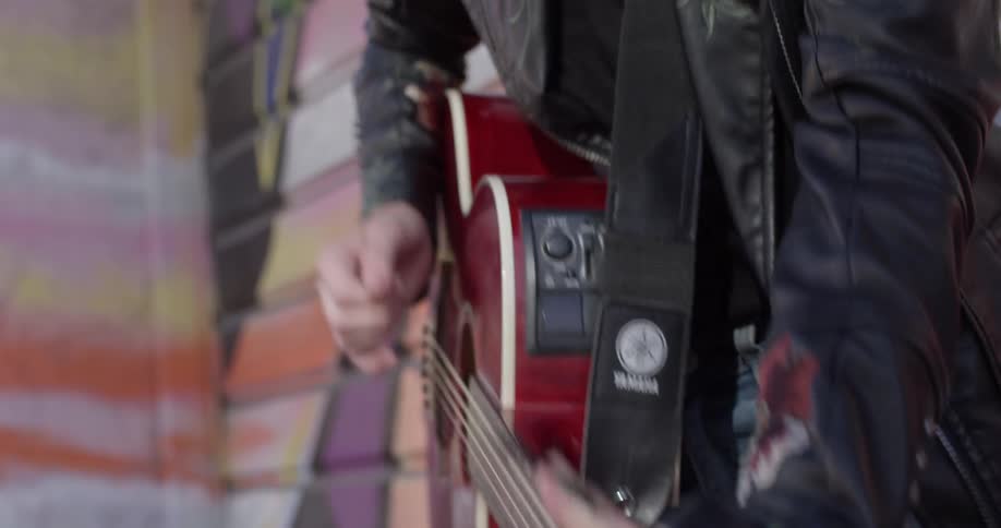 Woman playing a red guitar against a graffiti wall