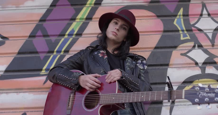 A woman standing in front of a painting holding a guitar