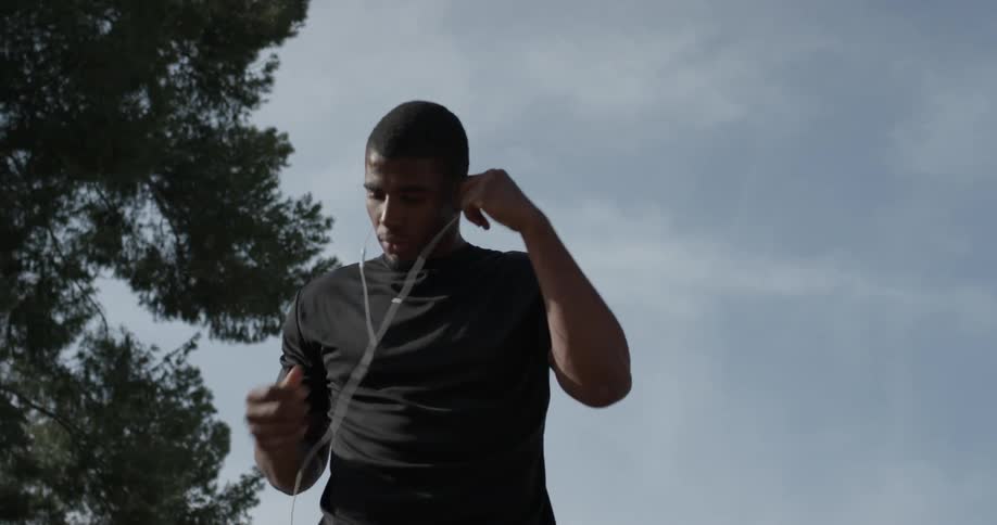 A man puts ear buds in his ears under a blue sky with wispy clouds