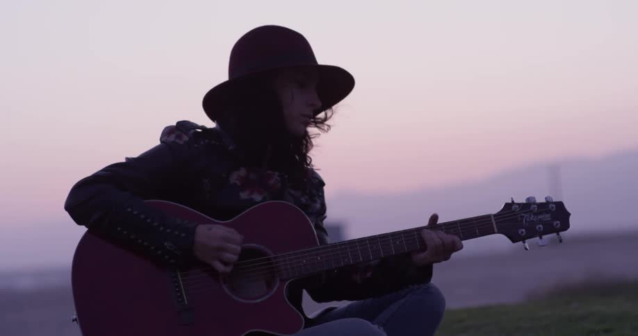 A woman plays a guitar on a beach at sunset