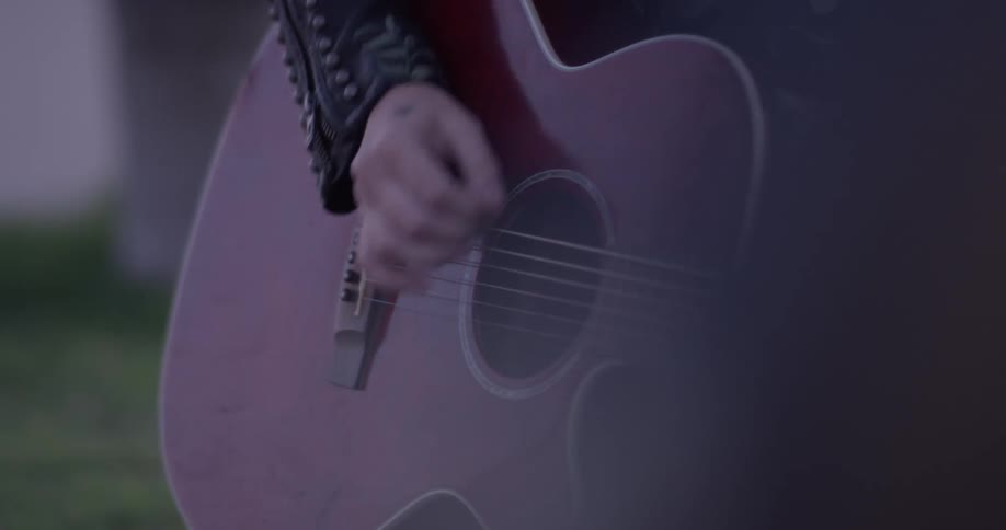 Woman strumming a guitar out on a grassy field