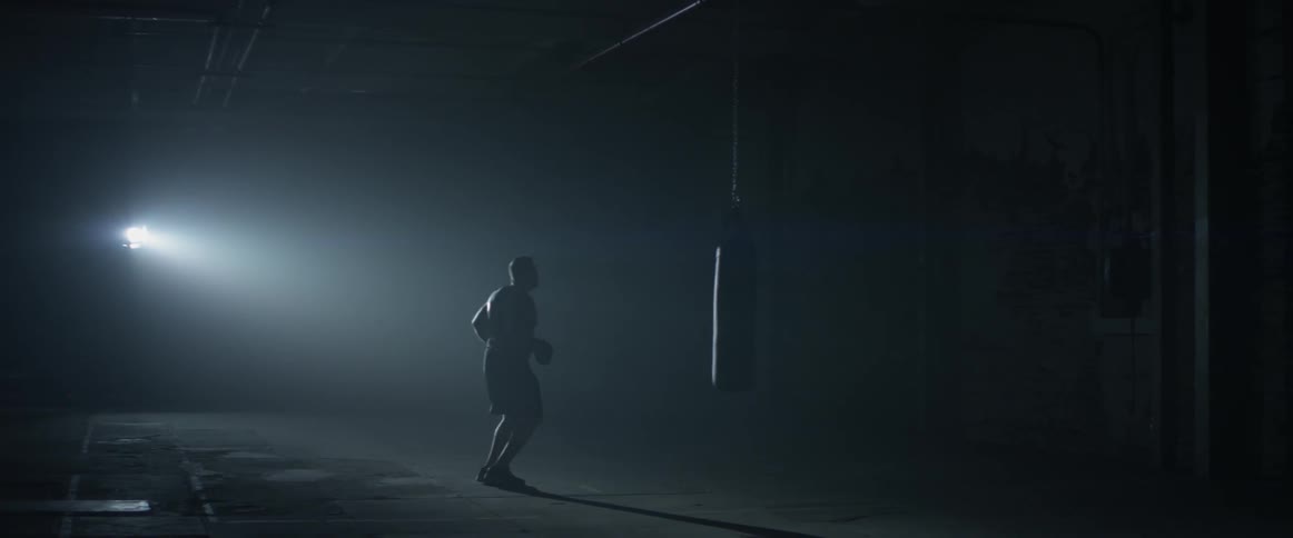 A man practices jabs in a dark gym before hopping to a punching bag