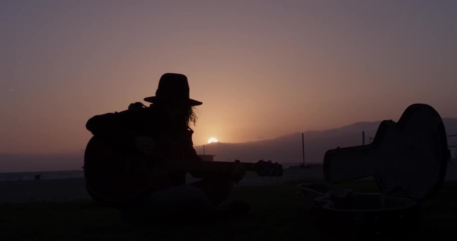 Woman plays guitar outdoors at sunset